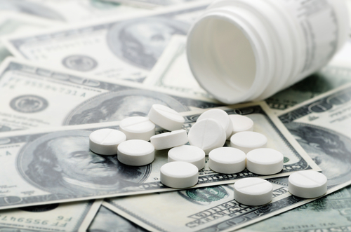 White pills, a common type of medication, are scattered on top of hundred-dollar bills next to an open white pill bottle.